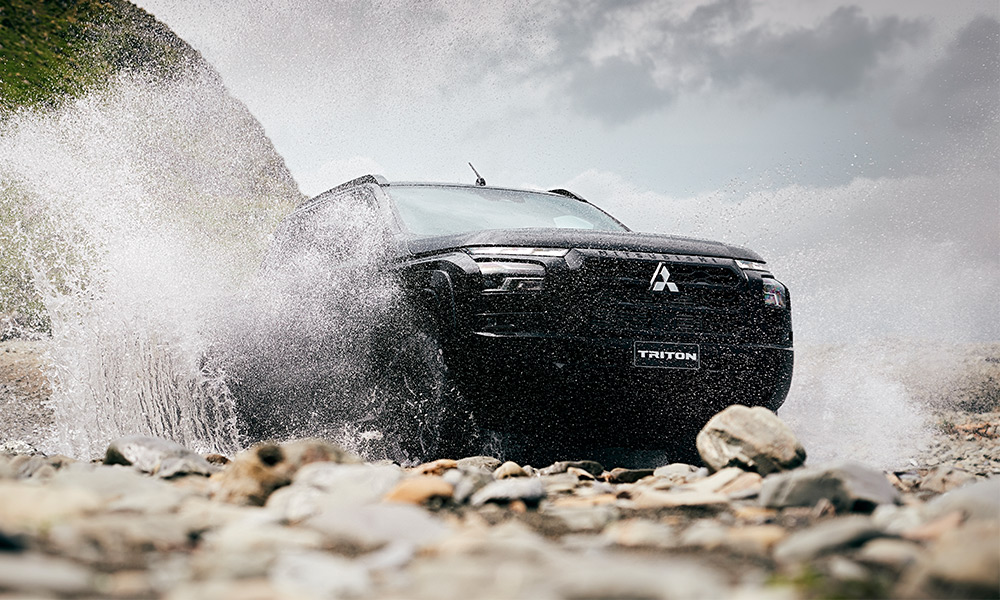A Black ute driving through a river and dirt