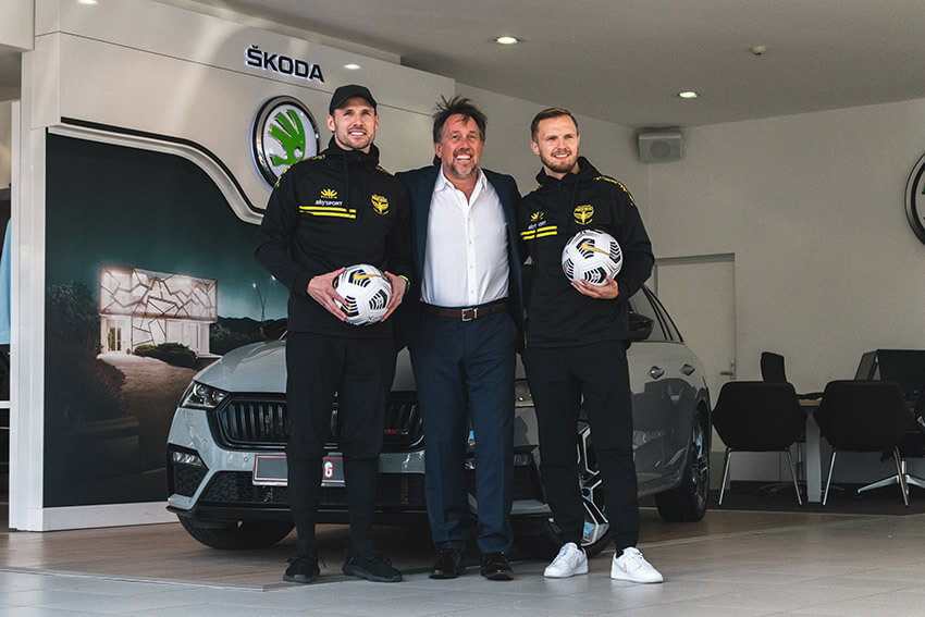 2 football players with a man in a suit in a Skoda showroom