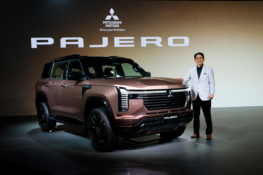 A man in a white suit standing next to a Mitsubishi Pajero SUV