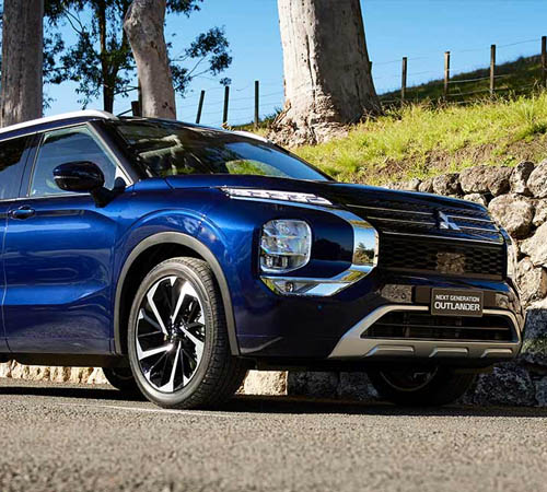 Blue Mitsubishi Outlander on paved road with mountains in the background