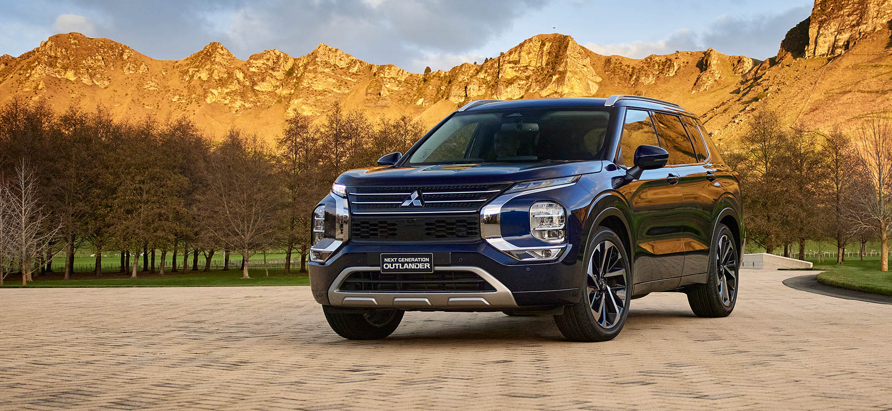 Blue Mitsubishi Outlander on paved road with mountains in the background